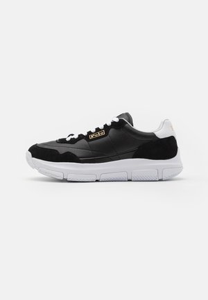 Black sneaker with a leather and suede upper, white sole, and contrasting accents. Features a gold logo and lace closure.
