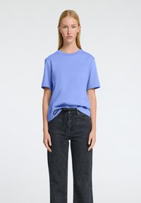 T-shirt en coton bleu clair avec un col rond et des manches courtes, associé à un jean en denim foncé taille haute avec un détail de cordon.