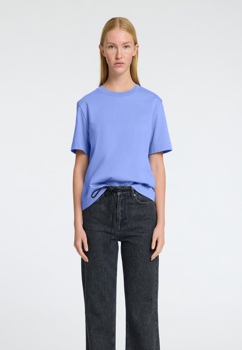 T-shirt en coton bleu clair avec un col rond et des manches courtes, associé à un jean en denim foncé taille haute avec un détail de cordon.