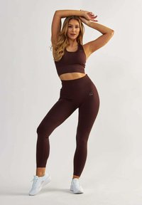 Hnědá žebrovaná sportovní souprava, která se skládá z crop topu a legín s vysokým pasem. Materiál je hladký s jemným logem. Doplňena bílými teniskami.