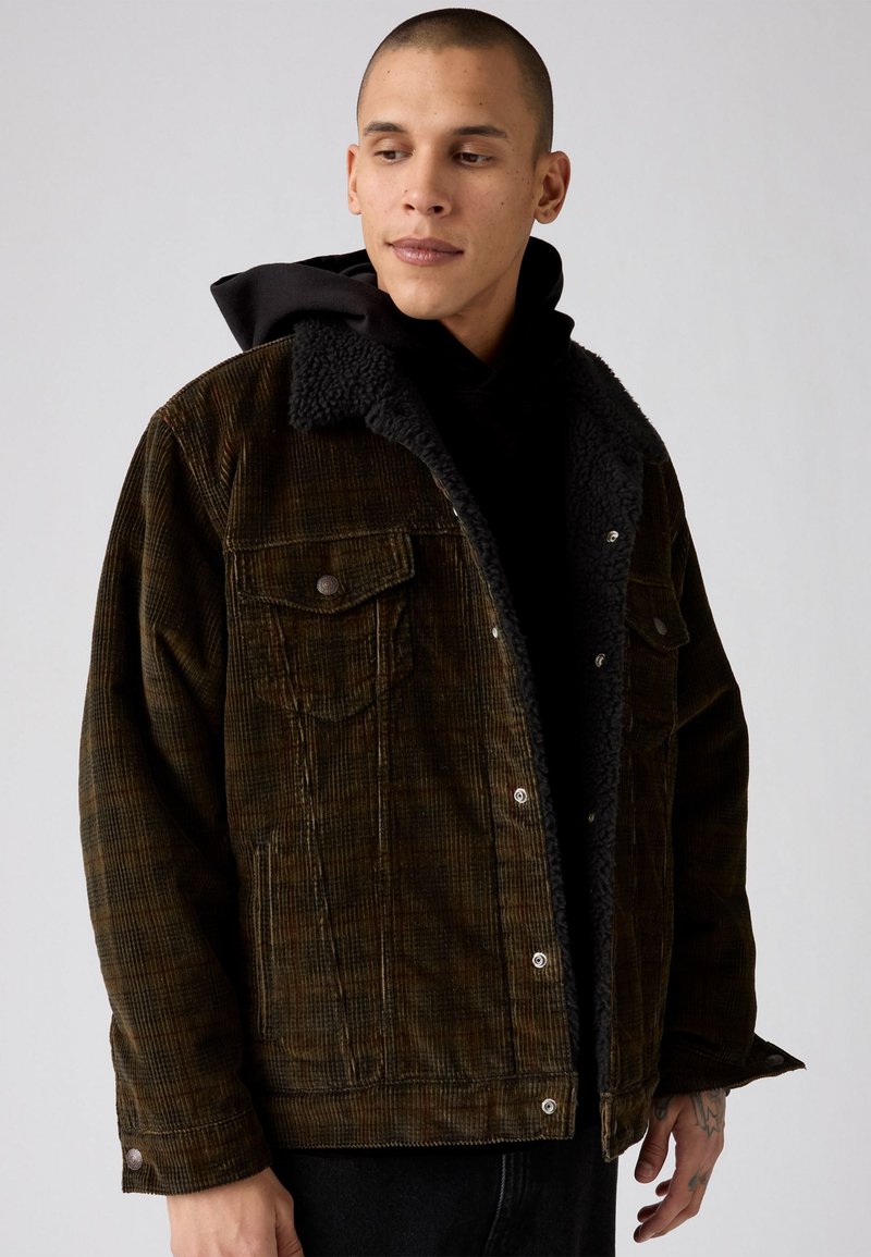 Brown corduroy jacket with a black fleece collar, featuring two front pockets, snap buttons, and a relaxed fit. Textured fabric with a check pattern.