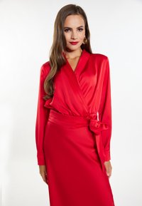 Abito avvolgente in satin rosso con maniche lunghe, vita legata e una texture morbida. L'abito è lungo fino al pavimento e presenta un profondo scollo a V.