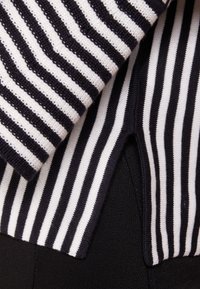 Tessuto a maglia a righe in bianco e nero, caratterizzato da linee diagonali con una finitura testurizzata. Messa a fuoco su motivi sovrapposti e bordi.