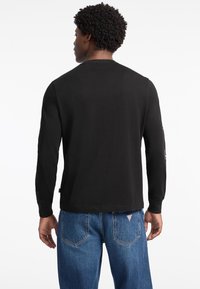 Sort langærmet skjorte med rund hals og en glat tekstur, parret med lyseblå jeans med en lap bagpå.