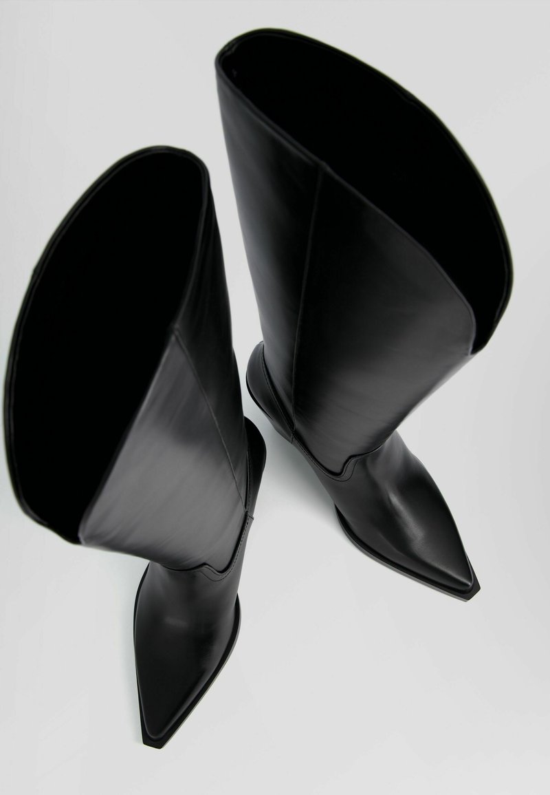 Bottes en cuir noir jusqu'au genou avec un bout pointu, texture lisse et une large ouverture en haut. Le design présente une silhouette élégante.