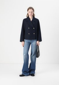 Veste navy croisée avec des boutons dorés. Associée à un jean évasé bleu clair déchiré. Sac à main noir avec bandoulière.