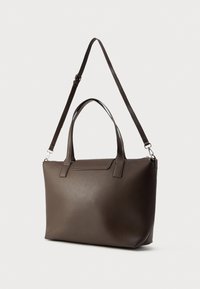 Σκούρο καφέ δερμάτινη τσάντα tote με διπλές λαβές και ρυθμιζόμενο ιμάντα ώμου, παρουσιάζεται πάνω σε ανοιχτό φόντο.