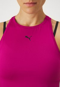 Närbild av en person som bär en ärmlös magenta sporttopp med en svart Puma-logga centrerad nära halsringningen.