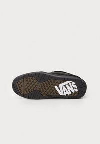 Semelle d’une chaussure Vans noire avec un motif gaufré et un grand logo Vans blanc sur le talon, sur fond uni.