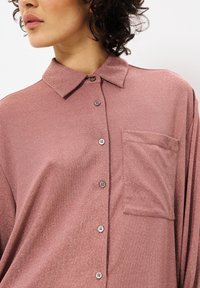 Knopfhemd aus weichem, schimmerndem Rosenstoff. Verfügt über einen Kragen, eine Tasche auf der Vorderseite und braune Knöpfe. Entspannt geschnitten mit glatter Textur.