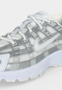 Λευκό και γκρι παπούτσι τρεξίματος Nike με ανώτερο μέρος από διχτυωτό υλικό, μαλακή σόλα και λευκά κορδόνια, με το λογότυπο Nike Swoosh στη πλευρά.