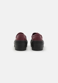 Burgundy platform sneakers with black rubber soles, textured leather uppers, and back heel loops for easy wear. Features Converse branding.