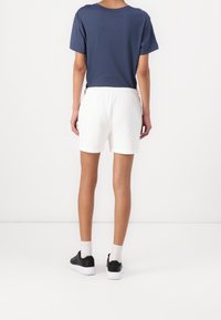 Witte shorts met een elastische tailleband, gecombineerd met een marineblauwe t-shirt. De outfit wordt aangevuld met zwarte sneakers en lichtgekleurde sokken.