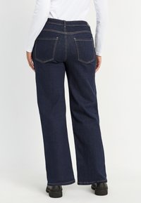 Hoge taille, donkerblauwe wijde jeans met zichtbare stiksels en twee achterzakken. Gemaakt van denim, met een ontspannen pasvorm en een effen kleur.