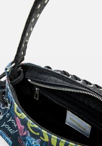 Reißverschlusstasche aus dunkelblauem Denim mit bunten Grafiken, ausgestattet mit einem strukturierten Riemen und metallischen Hardware, sowie einem markierten Innenetikett.