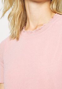 Różowy prążkowany t-shirt z dekoltem ozdobionym falbanką, o subtelnej błyszczącej fakturze. Krótkie rękawy i dopasowany krój.