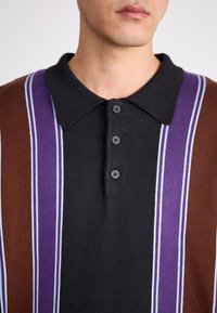 Polo à base noire avec des rayures verticales en marron, violet et bleu clair, en tissu texturé, avec une patte de boutonnage à trois boutons.