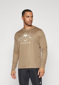 Hnedá športová košeľa s dlhým rukávom s textúrovaným grafickým dizajnom v svetlej béžovej farbe, s logom "ASICS FUJITRAIL" v strede. Hladká tkanina.
