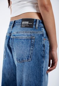 Blauwe denim jeans met een relaxte pasvorm, voorzien van een zwart etiket aan de achterzijde, gestikte zakomtrekken en een licht vervaagde textuur.