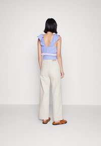 Top sem costas às riscas azul e branca com mangas em babados, combinado com calças largas de cintura alta de cor creme e sandálias castanhas.