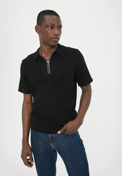 Polo shirt scurt negru, cu guler cu fermoar și o dungi colorate, având un design ajustat, asortat cu blugi texturați albaștri.