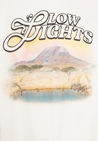 Camiseta blanca con una ilustración colorida de un paisaje montañoso con jirafas y cebras junto a un cuerpo de agua, y texto estilizado en la parte superior.