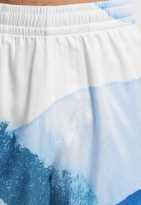 Plavky s bílým elastickým pasem. Látka má akvarelový vzor v světlých a tmavých odstínech modré. Hladká textura, lehký materiál.