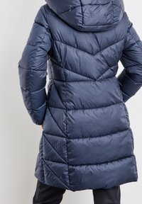 Marineblå pufferjakke med hætte. Quiltet design med chevron-mønstre. Glat, skinnende tekstur med en mellemlang længde.