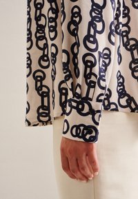Camicia a maniche lunghe in tessuto crema con un motivo a catena nera; dettagli con polsini abbottonati; texture liscia e vestibilità comoda.