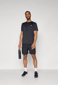 Musta urheilupaita ja shortsit, jotka on valmistettu kevyestä kankaasta. Oikeassa kädessä pidettävä musta vesipullo. Mustat lenkkarit. Minimalistinen muotoilu.