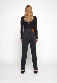 Svarta jeans i denim med hög midja, raka ben och en läderlapp på baksidan. Har subtila sömmar och en klassisk femficksdesign.