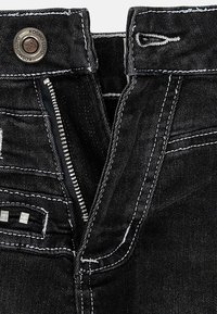 I jeans in denim nero presentano una chiusura con zip e un bottone metallico. Cuciture bianche accentuano le cuciture, con un'etichetta tessuta vicino alla vita.