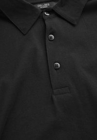 Svart polo skjorta i mjuk bomull, med klassisk krage, tre svarta knappar och en diskret sömdetalj.