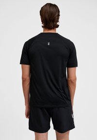 Zwart sportshirt met korte mouwen, gladde textuur en ronde hals. Heeft drie witte chevron-accenten op de bovenrug.