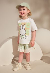 White t-shirt with Miffy graphic, green flowers. Green checkered shorts with white lace trim. Light green cap and white high-top sneakers.