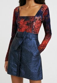 Haut à manches longues avec un décolleté carré, orné d'une surimpression en dentelle florale dégradée du rouge au violet. Mini-jupe en cuir bleu marine taille haute avec des boutons.