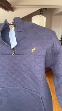 Gep quilteter navyblauer Pullover mit einem halben Reißverschluss und einem kleinen gelben, gestickten Vogel-Logo auf der linken Brust.