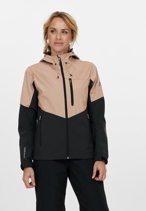 Veste pour femmes en matériau softshell ; présente un design bicolore beige et noir avec une capuche, des zips et des poches.