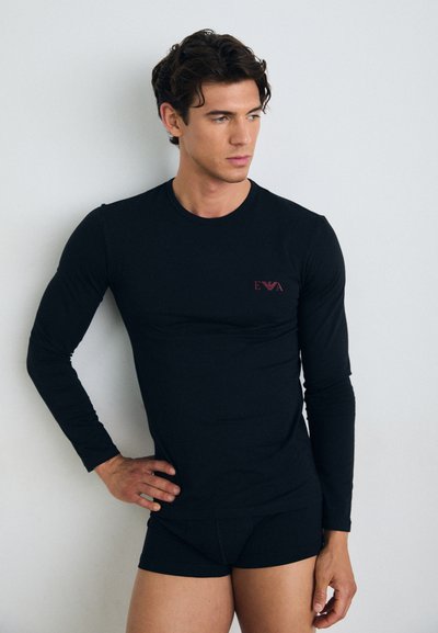 Chemise noire à manches longues en tissu doux, ornée d'un petit logo rouge. Associée à un short noir ajusté assorti. Design simple.