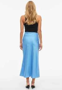 Lys blå satengklenning med glatt tekstur, vidde nederst og et kroppsnært livbånd. Brukt med en svart tanktop og flate sandaler.