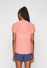 Růžové sportovní tričko s krátkým rukávem a designem s křížovými zády, s logem značky na horní části zad, v kombinaci s námořnickými šortkami se rozparkem.