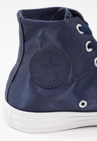 Sneaker Converse All Star montante bleu marine avec patch logo en tissu et semelle en caoutchouc blanche, vue de l'arrière.