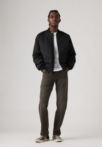 Chaqueta bomber negra con puños acanalados, camiseta blanca, pantalones verde oliva y zapatillas negras con suelas blancas. Fondo neutro.