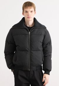 Black puffer jacket featuring a high collar, quilted texture, and front zipper. It has elastic cuffs and two side pockets.