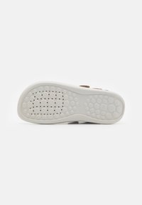 Suela de zapatilla con una base de goma blanca texturizada que presenta patrones circulares y perforados para mayor agarre y flexibilidad.