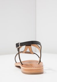 Sandal in pelle nera con cinturini sottili, fibbia in argento e suola in legno naturale. Presenta una texture liscia e un design minimalista.
