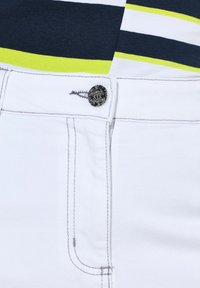 Pantalones cortos de mezclilla blanca con cierre de botón plateado, que presentan costuras en contraste en gris y una textura de tela suave. Rayas horizontales visibles en la parte superior.