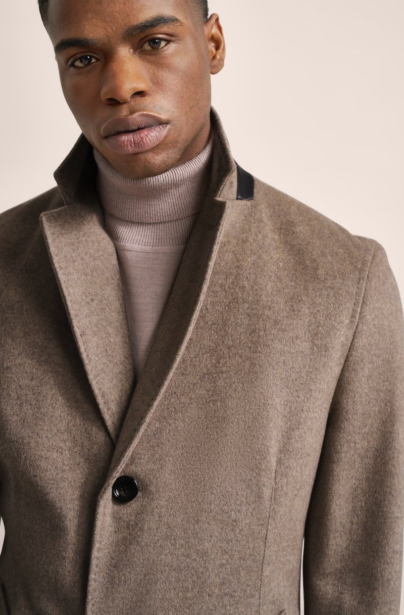 Cappotto in misto lana marrone con colletto alto, chiusura con un singolo bottone nero e finitura testurizzata, indossato sopra un dolcevita rosa chiaro.