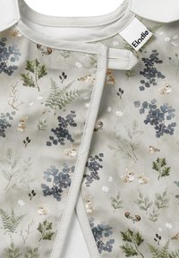 Blommönstrad tyg med beige bakgrund som visar kaniner, blad och små fåglar. Accentuerad med ljusgrå trim och en etikett.