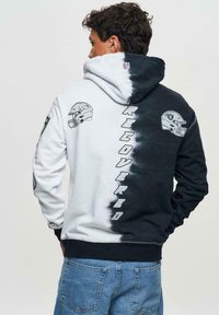 Sweatshirt à capuche avec un dégradé noir à blanc, comportant des graphiques de casques NFL et le texte "RÉCUPÉRÉ" au dos, capuche ajustable.